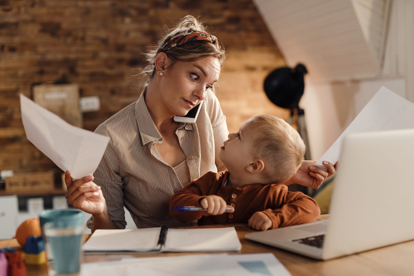 Multi-tasking working mother with small son at home. Single mother talking on the phone and going through paperwork while looking at her small son who is sitting on her lap.